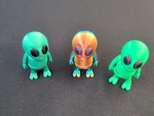 Three small 3D-printed alien figures in green, teal, and orange
