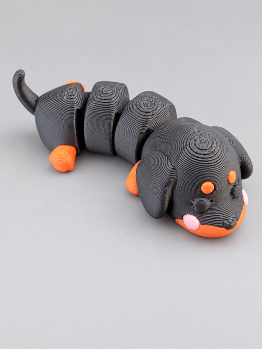 Articulated 3D printed dachshund in charcoal gray with orange and pink accents