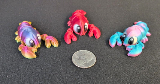 Three colorful 3D printed lobster toys beside a U.S. quarter for scale