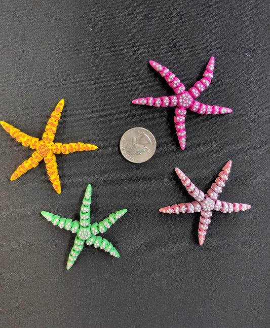 Four colorful 3D printed starfish beside a quarter for scale