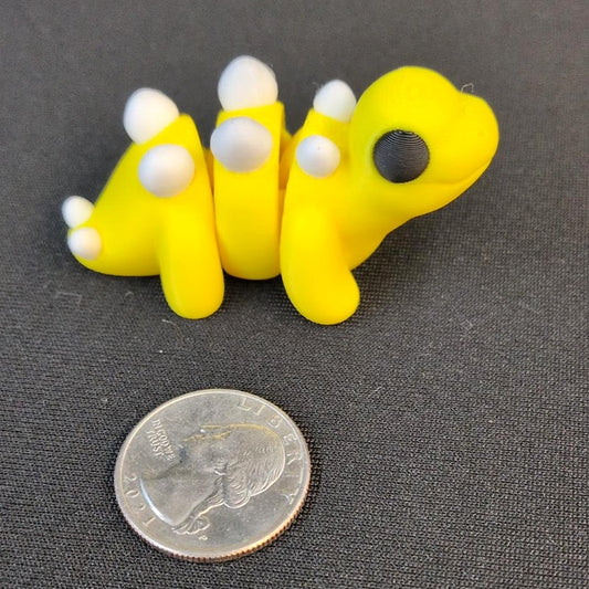 Yellow articulated 3D printed Stegosaurus with white plates beside a quarter for scale